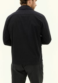 Giacca di cotone blu navy con collo classico, linee pulite e maniche lunghe, che mostra una trama minimale e dettagli di cucitura sottili.