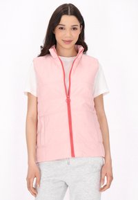Gilet imbottito leggero rosa con colletto alto e zip frontale. Accentuato da una zip corallo brillante. Indossato sopra una maglietta bianca.