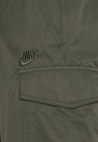 Olivově zelené cargo šortky Nike s výrazným vyšitým logem, několika kapsami a odolnou texturou látky.
