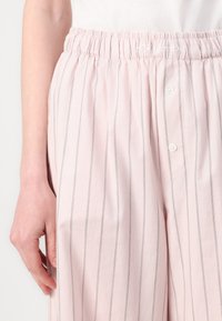 Lyserøde stribede bukser har en elastisk talje med syningdetaljer og forreste knaplukninger. Stoffet virker let og åndbart.