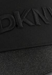 Gorra negra con logotipo bordado en relieve y una textura brillante en el visor, con una parte superior lisa y sutilezas en las costuras.