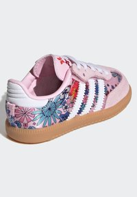 Zapatilla deportiva rosa con un diseño floral con acentos azules y morados, franjas blancas, ante suave y suela de goma, cuello acolchado y cordones.