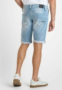 Pantalones cortos de mezclilla azul claro con dobladillos enrollados, cinco bolsillos y un parche rectangular de cuero negro en la cintura trasera.