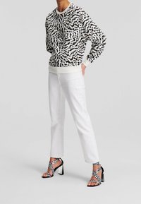 Musta-valkoinen kuvioitu pusero pitkillä hihoilla, yhdistettynä valkoisiin suoralahkeisiin farkkuihin ja mustiin nilkkaremmillä varustettuihin korkokenkiin.