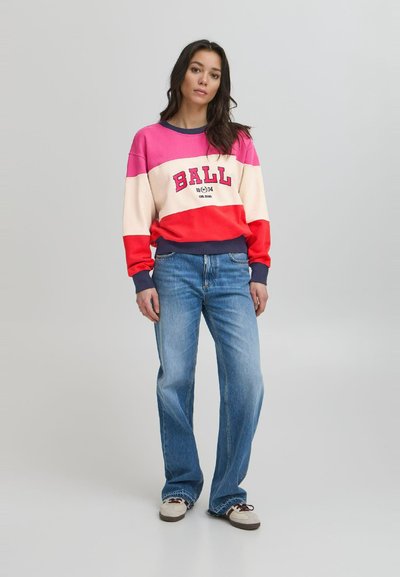 Fargerik hettegenser med horisontale striper i rosa, krem og rødt, med ordet "BALL" i fet tekst, paret med lyseblå vide jeans.