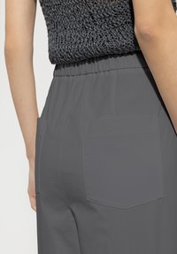 Gray pants with a smooth texture feature an elastic waistband and two square pockets. The fabric appears lightweight and breathable.