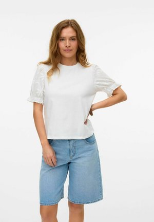 T-shirt en coton blanc avec des manches bouffantes brodées, associé à un short en denim bleu. Le T-shirt a une coupe décontractée et un col rond.