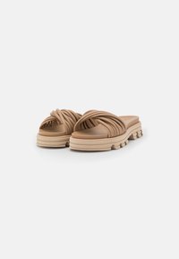 Sandales en caoutchouc moulé beige, avec des lanières tressées, une semelle épaisse et rembourrée, et des stries texturées pour une meilleure adhérence. Design à bout ouvert sans fermetures.