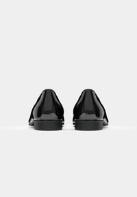 Scarpe in pelle verniciata nera con un design elegante e arrotondato, suole piatte, che presentano superfici lisce e lucide e contorni ergonomici.