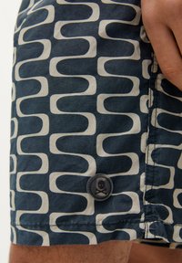 Shorts de bain navy avec un motif de vagues ivoire, fabriqués en tissu léger, ornés d'un bouton circulaire embossé d'un design de crâne.