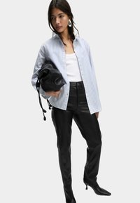 Camisa de botones a rayas en azul y blanco, llevada sobre una camiseta sin mangas blanca, combinada con pantalones de cuero negros de cintura alta y un bolso negro.