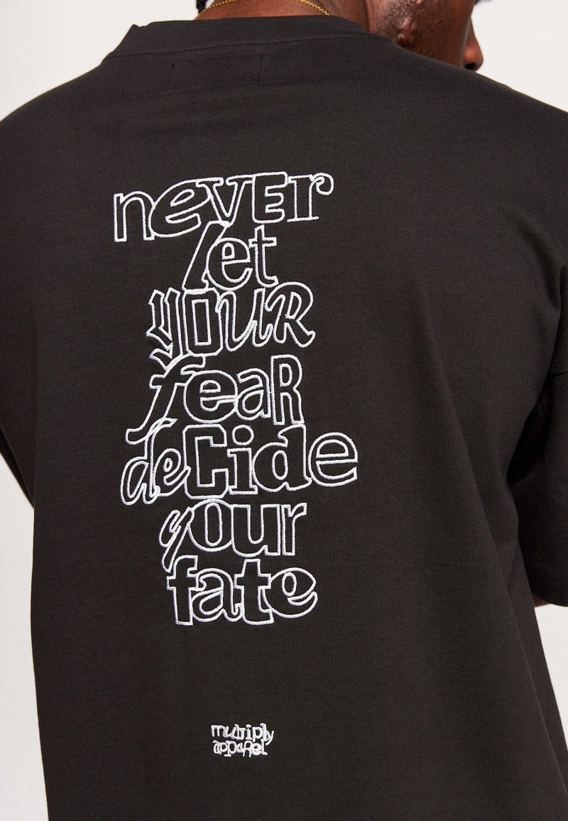 Black cotton t-shirt featuring white embroidered text on the back: "never let your fear deCide your fate" with a small logo at the bottom.