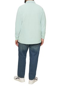 Jasno miętowa polo z długim rękawem z kołnierzykiem, w połączeniu z niebieskimi dżinsami o luźnym kroju i białymi sneakersami z czarnymi akcentami.