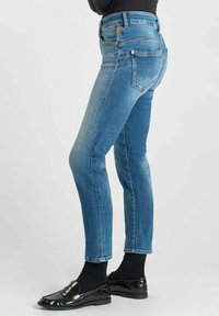 Jeans skinny en denim bleu avec une taille mi-haute, un design classique à cinq poches et une décoloration subtile. Associés à des mocassins noirs et des chaussettes.