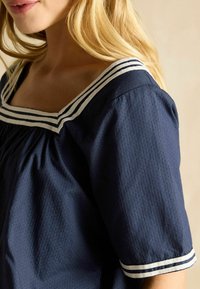 Bluza bleumarin dintr-un material texturat, cu decolteu pătrat, având o margine cu dungi albe pe guler și mâneci.