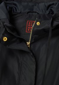 Black waterproof jacket with a gold zipper and snap closures; features soft inner lining and a red label. Smooth texture, no visible patterns.