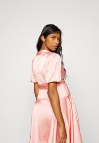 Vestido de cetim rosa com mangas bufantes, cintura ajustada e saia fluida. Apresenta uma gola e textura suave, criando uma silhueta elegante.
