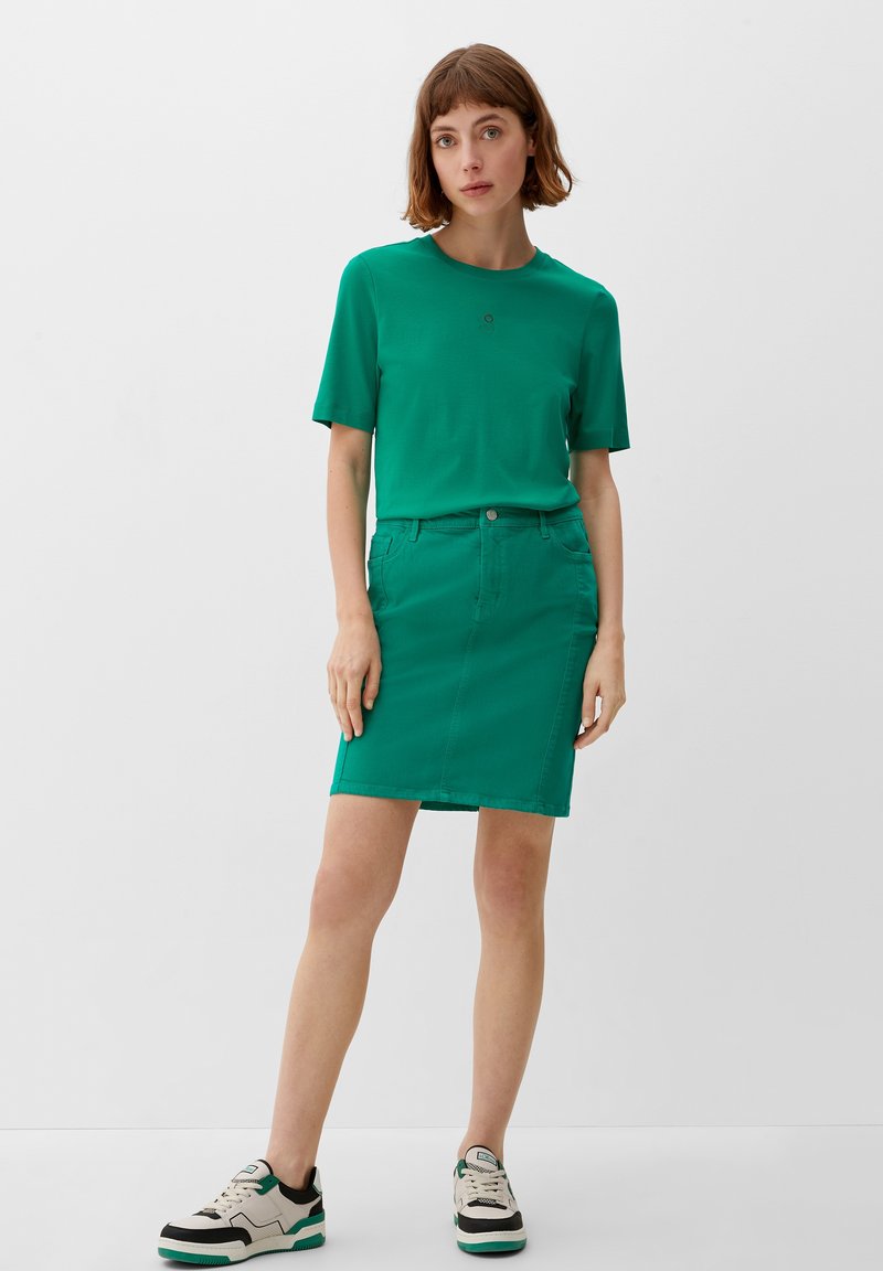 T-shirt vert et jupe en denim assortie. L'ensemble présente un col rond, des manches courtes et des lignes épurées, associé à des chaussures décontractées.