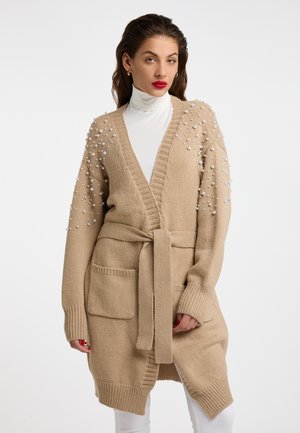 Beige Strickjacke mit Perlenakzenten an den Ärmeln, einem Gürtel zum Binden, Fronttaschen und einem V-Ausschnitt. Weicher Stoff und mittellange Länge.