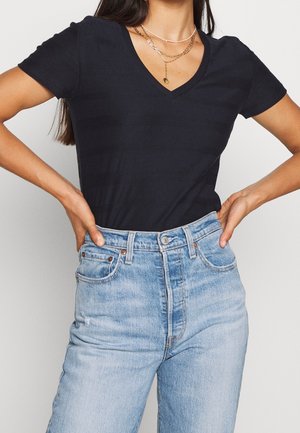 Granatowy T-shirt z dekoltem w serek wykonany z miękkiej tkaniny, zestawiony z jasnoniebieskimi jeansami z wysokim stanem, ozdobionymi wyblakłymi detalami i klasycznym designem z pięcioma kieszeniami.