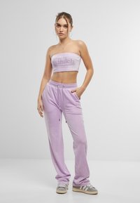 Lilla fløyels to-delt antrekk med en stroppeløs topp med logo og matchende joggebukser med snøring i livet og sidelommer.