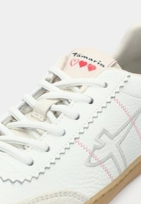 Λευκά αθλητικά παπούτσια με κορδόνια, από δέρμα στην επάνω επιφάνεια, με κυματοειδή άκρη, ανοιχτό γκρι λεπτομέρειες, ροζ κεντήματα και λογότυπο στη γλώσσα που περιλαμβάνει καρδιές.