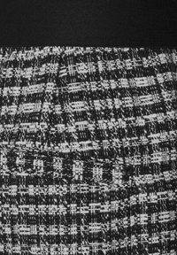 Svart och vit tweedtyg med en strukturerad mönster och elastisk midjeband. Har vävda linjer som skapar en strukturerad design.