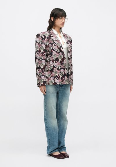 Φλοράλ σακάκι σε σκούρο κόκκινο, συνδυασμένο με ανοιχτό μπλε τζιν παντελόνι με φαρδιά μπατζάκια. Το μοντέλο φορά μπορντό μπαλαρίνες και στρογγυλά γυαλιά. Λείο ύφασμα.