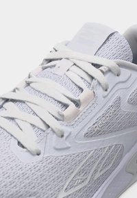 Κοντινό πλάνο σε ένα λευκό αθλητικό παπούτσι Reebok που δείχνει υφασμάτινη υφή, κορδόνια δεμένα σε φιόγκο και το λογότυπο της μάρκας στο πλάι.