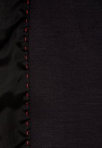 Schwarzer Stoff mit glatter Textur, der einen gekräuselten Rand und rote Nähte entlang einer Seite aufweist und Kontrast sowie Detail zeigt.
