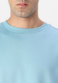Világoskék kerek nyakú t-shirt, puha anyagból, sima textúrával és formához illeszkedő fazonnal, egyszínű dizájnnal, látható minták nélkül.