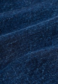 Tela de mezclilla oscura que muestra una superficie texturizada con diferentes tonos de azul. El material tiene un ligero brillo y patrones de tejido visibles.