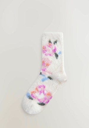 Bolyhos fehér zokni színes virágmintákkal rózsaszínben, narancssárgában, kékben és feketével. Puha textúrájú, testhezálló alakú, lekerekített orrú.