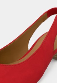 Κόκκινο σουέτ γυναικείο παπούτσι slingback με εσωτερικό σε φυσική απόχρωση, χαμηλό τακούνι και ανοιχτό κομμένο σχέδιο στο πλάι. Ομαλή υφή σε όλο το παπούτσι.