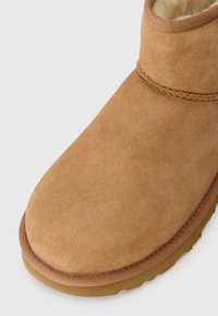 Tan suede nilkkabootit pyöreällä varvalla ja ommellulla reunuksella. Pehmeä, ylellinen vuori ja näkyvä kumipohja, suunniteltu mukavuutta ja lämpöä varten.