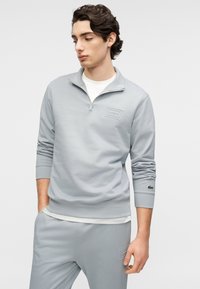 Ανοιχτό γκρι φούτερ με φερμουάρ, με μινιμαλιστικό σχέδιο, που διαθέτει μικρό λογότυπο σε ταμπέλα, ριμπ μανσέτες και ομαλή υφή.