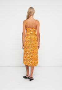 Vestido midi amarelo de flores com alças finas ajustáveis, corpete justo e saia fluida, apresentando um padrão vibrante de pequenas flores.