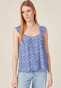 Top de tirantes azul con estampado floral, con mangas rizadas y escote redondo, hecho de tela ligera, combinado con jeans de un azul claro.