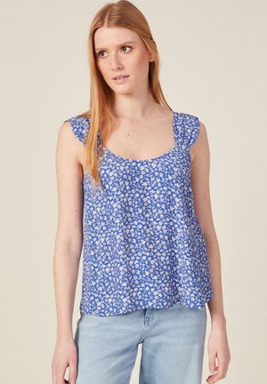 Top senza maniche a fantasia floreale blu con maniche a volant e scollo a barca, realizzato in tessuto leggero, abbinato a jeans azzurri.