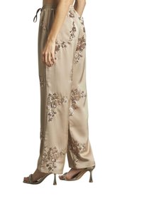 Pantalon en satin beige avec broderie florale en bronze et paillettes. Doté d'une taille élastique et de poches latérales. Design à jambe évasée.