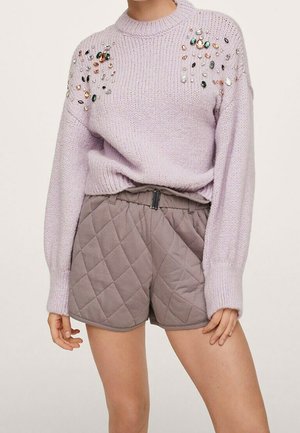 Fioletowy sweter z dzianiny z wielokolorowymi koralikami na ramionach, w połączeniu z wysokim stanem pikowanych krótkich spodenek w kolorze taupe.