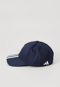Marineblå caps med flat skygge, med tre hvite striper på visiret og et brodert logo på fronten. Stofteksten er jevn.