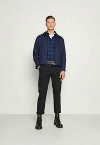 Tumesinine bomber-jakk mustrilise särkide peal, mustad püksid ja mustad sõjaväejalatsid. Sile kangas, kohandatud sobivus ja lukuga sulgemine.