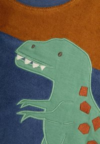 Zaļš dinozaura izšuvums uz auduma ar ziliem un brūniem laukumiem. Dinozaurs izceļas ar asiem zobiem un brūniem sešstūra akcentiem.