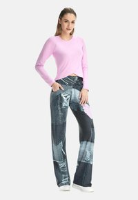 Hellrosa langärmeliges Oberteil mit abgerundetem Saum, kombiniert mit weitem Denim-Hosen mit Patchwork-Design in verschiedenen Blautönen.