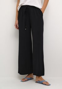 Zwarte wijde broek met een trekkoord in de taille, gemaakt van zachte stof. Heeft zijzakken en een ontspannen pasvorm, geschikt voor casual dragen.