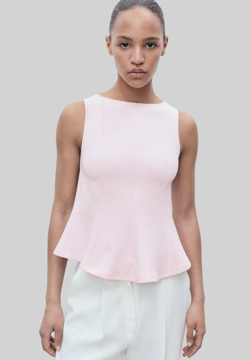 Top senza maniche di un delicato rosa pallido, corpino fitted con orlo svasato, texture liscia e dettagli di cucitura sottili. Abbinato a pantaloni bianchi.