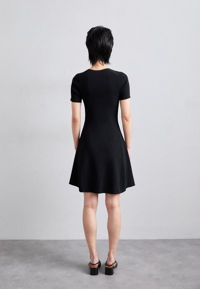 Rochie neagră cu mâneci scurte, cu un corset ajustat și fustă evazată. Textură răsucită, lungime deasupra genunchiului, asortată cu sandale cu toc gros.