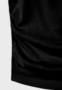 Musta kangas, jossa on hienovarainen poimutettu rypytys sivusauman varrella, yksinkertaisen vaalean taustan edessä.