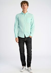 Jasnoniebieska, długosleeve koszula z guzikami z kieszenią na piersi, zestawiona z ciemnymi dżinsami i białymi trampkami z wielokolorowymi akcentami.